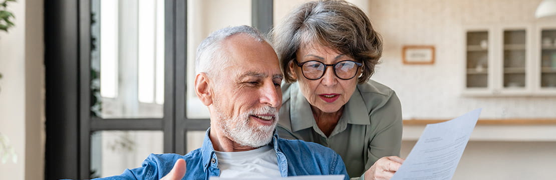 Caucasian senior spouses reading paperwork.